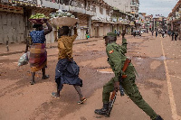 A police officer beats a female orange vendor on a street in Kampala, | BADRU KATUMBA | AFP