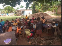 The KG pupils having lessons under trees and using logs as chairs