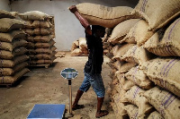 A worker transports a bag of sun-dried cocoa beans at a warehouse [REUTERS/Francis Kokoroko]