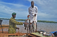 A Fisheries Protection Unit officer and a fishermen display fish on the shores of Lake Victoria