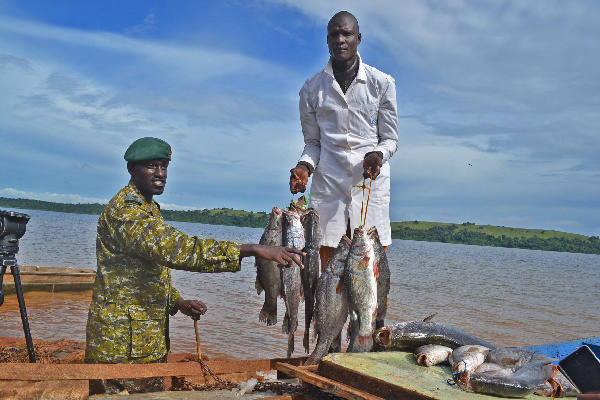 A Fisheries Protection Unit officer and a fishermen display fish on the shores of Lake Victoria