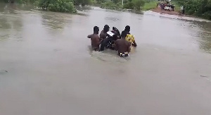 Men carrying a motorcycle across a flooded road