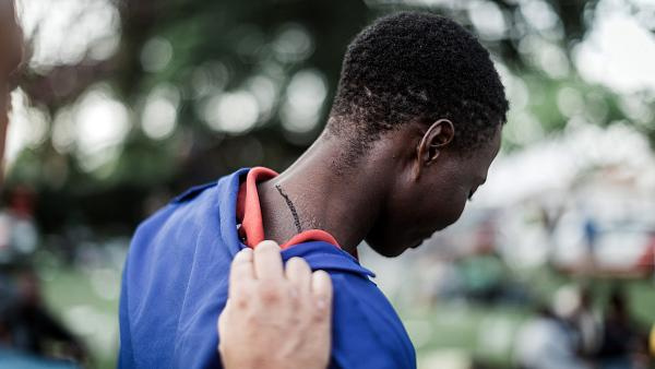 A person shows a scar on his neck as he takes refuge outside a local park near the Sydenham Police