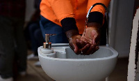 A man washes his hands at a public hand washing station before boarding a bus