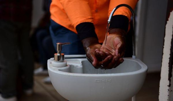 A man washes his hands at a public hand washing station before boarding a bus