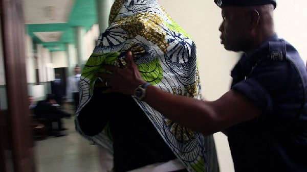 A woman enters the High Court in Accra covered in African print material ,with the help of a police