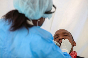 A medical worker wearing PPE takes a swab sample from a man