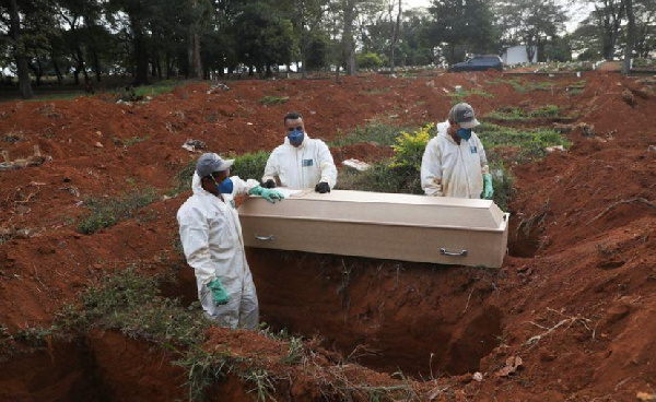 Gravediggers wearing protective suits prepare to bury the coffin of a person who died from the virus