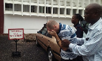 David McDermott hides from cameras as he is being escorted from the court premises in Accra