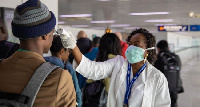 An airport official takes temperature of an arriving passenger