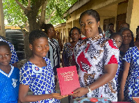 Akosua Manu presents a copy of donated books to a pupil