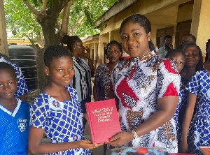 Akosua Manu presents a copy of donated books to a pupil