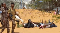 Four blindfolded journalists lie on the ground as police walk by in Somalia