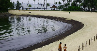 Beach-goers walk next to the polluted oil slick at Tanjong Beach on Sunday