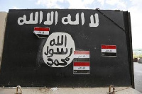 A man stands in front of the traditional black flag of Islamic State insurgents. [Reuters]