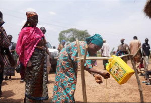 Women washing hands under tippy tap, men installing tippy tap