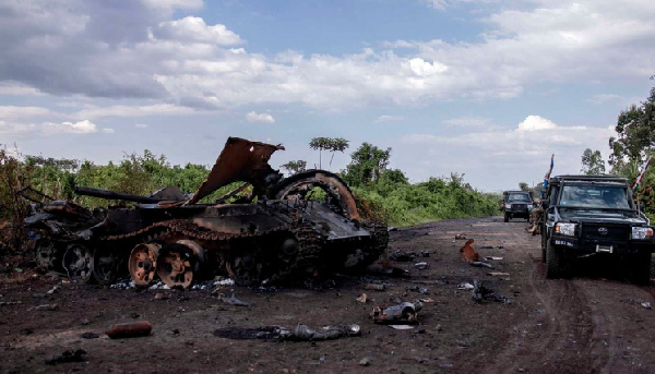 Cars passing by a destroyed military vehicle in Rugari