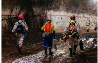 Miners wearing safety equipment walk through an underground tunnel at the South Deep gold mine