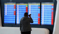 A man stands in front of a screen showing that multiple departure flights have been cancelled