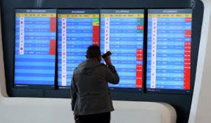 A man stands in front of a screen showing that multiple departure flights have been cancelled