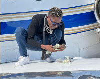 Dancehall artiste, Shatta Wale counts money on the wing of an aircraft