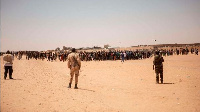 Nigerien soldiers stand guard as a crowd of migrants gather in Assamaka