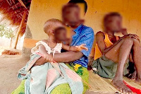 A victim of child marriage carrying a baby. Sitting with her is her husband