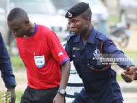 A Ghanaian referee being escorted out of the field after a match