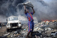 Boy lifts up cathode ray tube from damaged monitor on a rubbish dump.