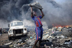 Boy lifts up cathode ray tube from damaged monitor on a rubbish dump.