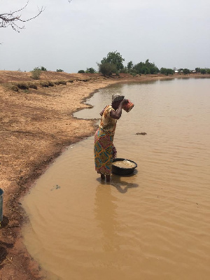 An old woman from Tolon drinks water from the pond