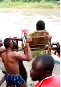 A pregnant woman being carried in a chair across the river