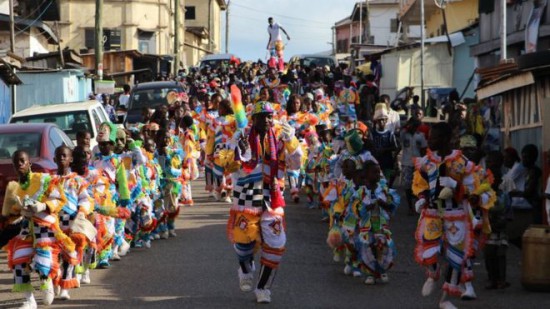 Lines of children parade in the street wearing multi-coloured feather outfits, led by an adult male. In the background, a man on stilts balances in the crowd.
More than 1,000 people lined the streets to celebrate Easter in Ghana's small port city of Sekondi